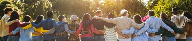 diverse group of people standing together in a line with arms around each other and looking at the sunset