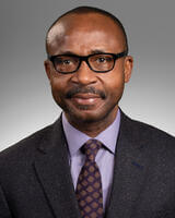 Chukwuma Ogugua in dark suit with purple shirt wearing glasses with short dark hair