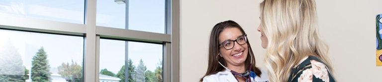 healthcare professional with a stethoscope listening to a patinets heart near a window
