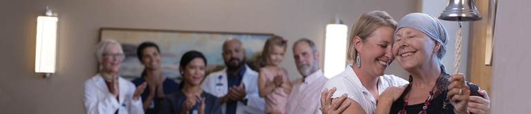 Breast cancer survivor ringing a bell while being encouraged by doctors and family.