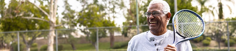 Senior African American man smiling while holding his tennis racket.
